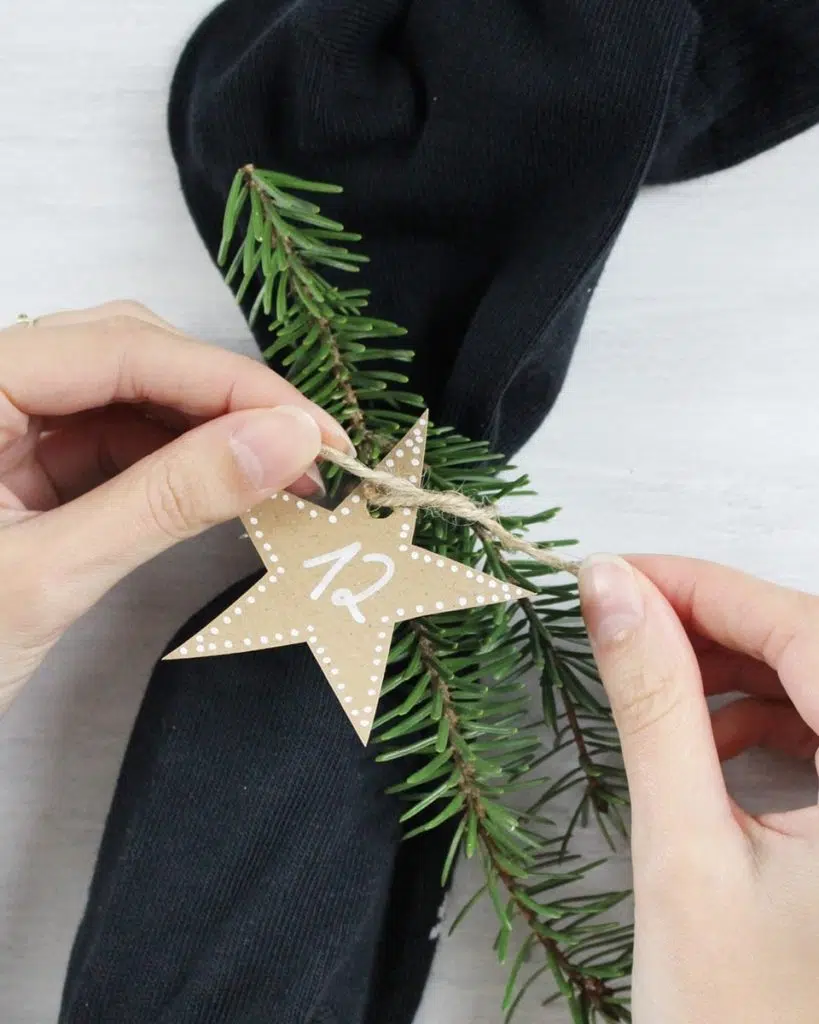 Du möchtest dieses Jahr einen DIY Adventskalender verschenken? Ich habe eine schöne und zugleich praktische Idee für dich! Du kannst einfach 12 Paar Socken mit Kleinigkeiten befüllen. So sparst du dir das Verpackungsmaterial und die kleinen Geschenke sind super schnell verpackt. Zusätzlich habe ich kleine süße Anhänger für die Zahlen gebastelt und etwas Tannengrün an den kleinen Päckchen festgebunden. DIY Adventskalender aus Socken basteln | Tinkerhome - einfache DIYs für Zuhause