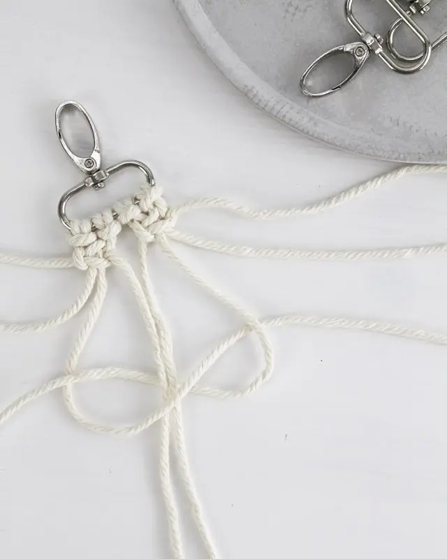 Makramee ist weiterhin im Trend und neben den klassischen Wandbehängen gibt es viele weitere Anwendungsmöglichkeiten. Im letzten Jahr habe ich mir sogar eine eigene Handtasche geknüpft. Vor ein paar Wochen bin ich nach Paris gereist und dafür brauchte ich eine kleine Umhängetasche, die ich gut vorne tragen kann. Parallel knüpfte ich an einem anderen Makrameeprojekt: einem Makramee-Übertopf mit dickerem Makrameegarn. Dabei kam mir die Idee, dass ein DIY Makramee Schultergurt aus diesem dicken Makrameegarn sicherlich toll aussähe. Also habe ich mich auf die Suche nach einer passenden Umhängetasche begeben, bei der ich den Schultergurt einfach abmachen kann, um später meinen eigenen Makramee Schultergurt daran zu befestigen. So kann man die Schultergurte beliebig wechseln. DIY Makramee Schultergurt knüpfen - 4 Anleitungen - diy schultergurt handtasche knuepfen kreuzknoten 21