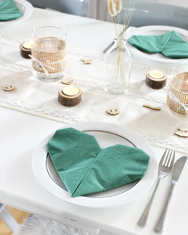 Statt kitschiger Plastikdeko kannst du deine Oktoberfest Tischdeko selber machen – rustikal, gemütlich und mit echtem Almcharakter. Viele greifen zwar schnell zu weiß-blauen Rauten und Einweg-Plastik, doch umwelttechnisch ist das kein Hit – und die Stimmung wirkt oft eher billig als festlich. DIY Oktoberfest Tischdeko basteln - Servietten zu Herz falten | Tinkerhome - Einfache DIYs für dein Zuhause